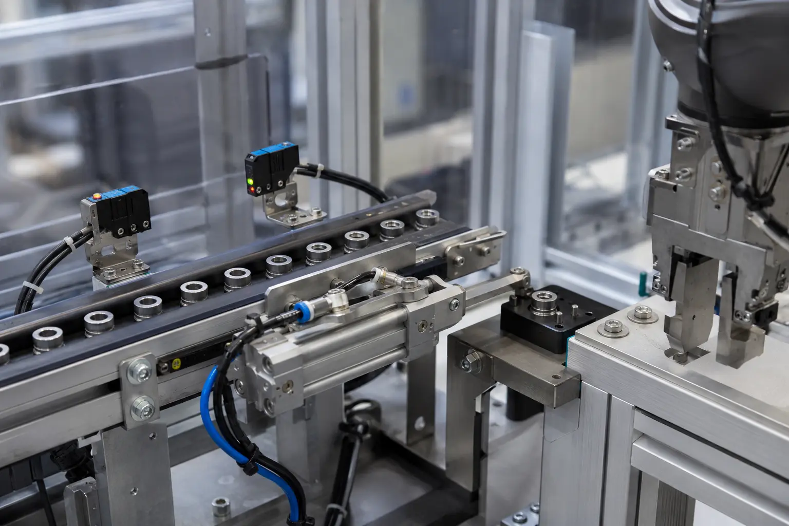 Ring-shaped components on a track beside sensors and a pneumatic cylinder.